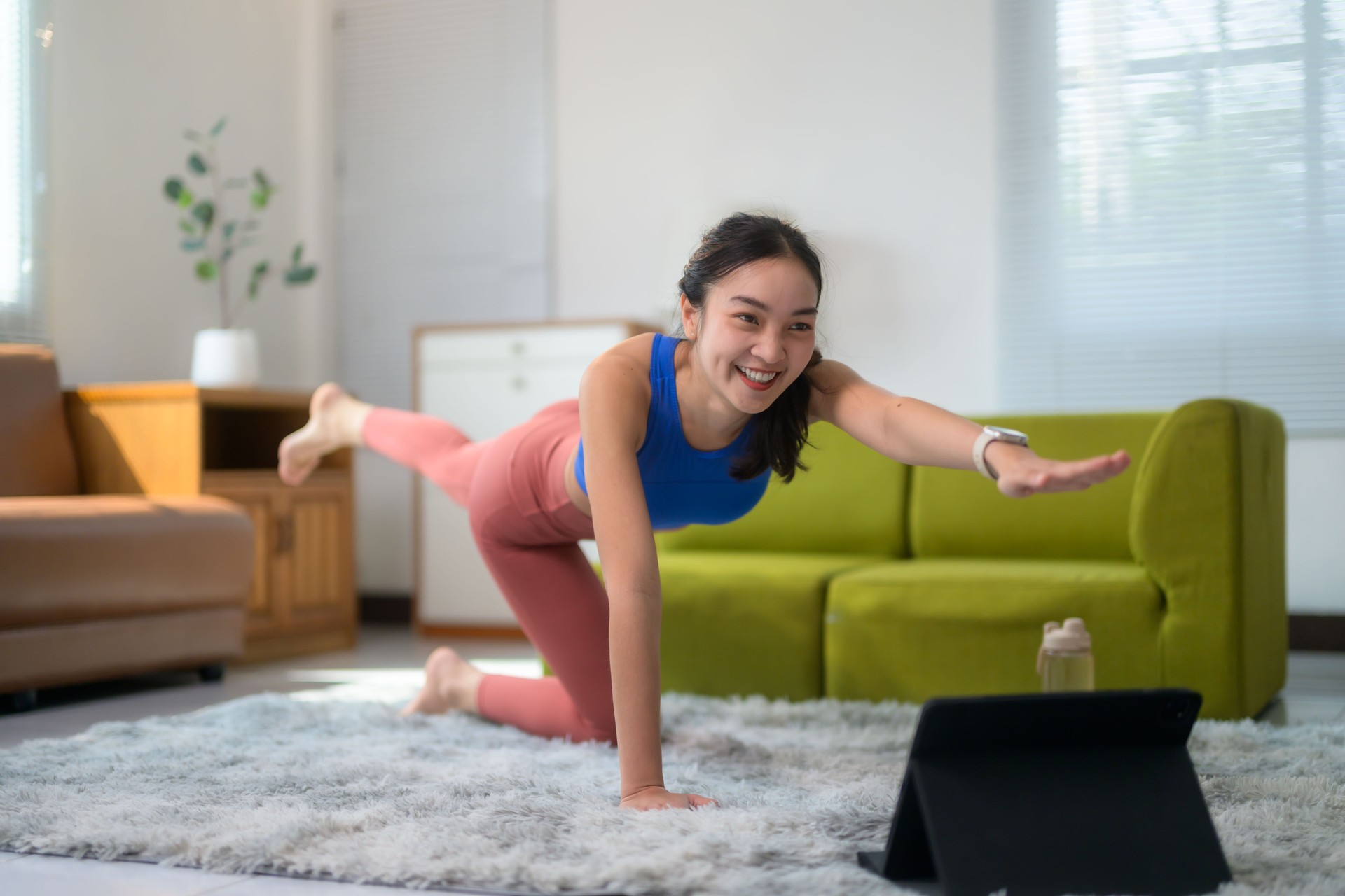 Young asian woman practicing yoga at home, following an online class on her tablet, performing the bird-dog pose in her cozy living room, embracing fitness and wellness